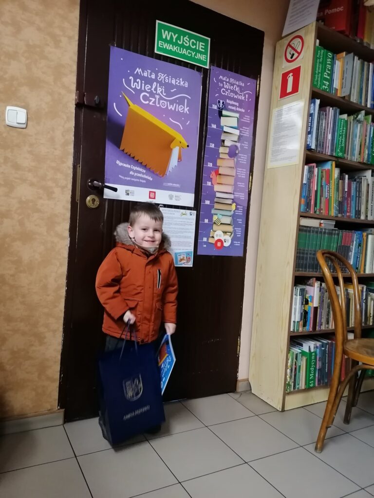 zadowolony chłopiec w pomarańczowej kurtce trzyma ogromną nagrodę