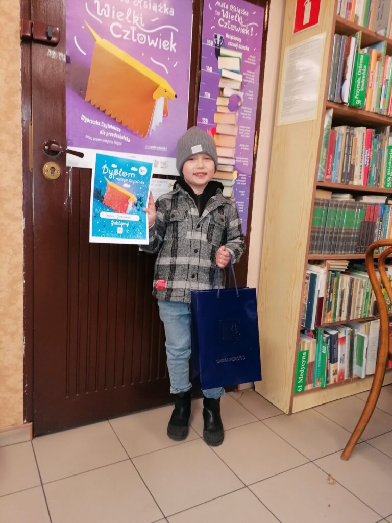 zadowolone dziecko stoi przed drzwiami z dyplomem w ręku
