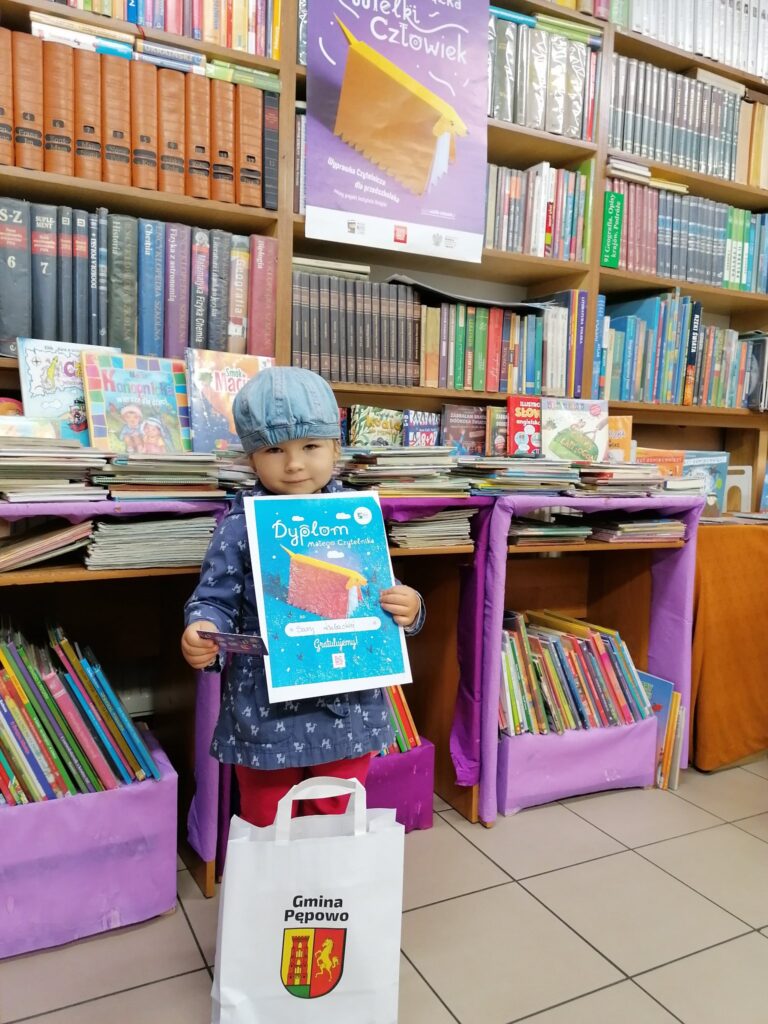 zadowolone dziecko stoi przed drzwiami z dyplomem w ręku na tle książek