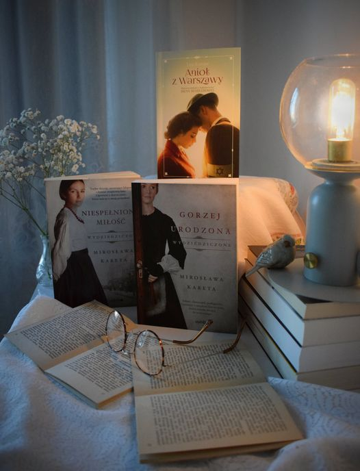 romantyczna seria książek na stoliku nocnym z zapaloną lampką i okularami
