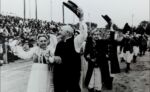 Gminne dożynki na stadionie w Pępowie 15 września 1985 rok ph. ,,Otwórzcie szeroko wrota, bo się zakończyła żniwna robota". zespół taneczny w strojach ludowych wiwatuje czapkami i pozdrawia publiczność